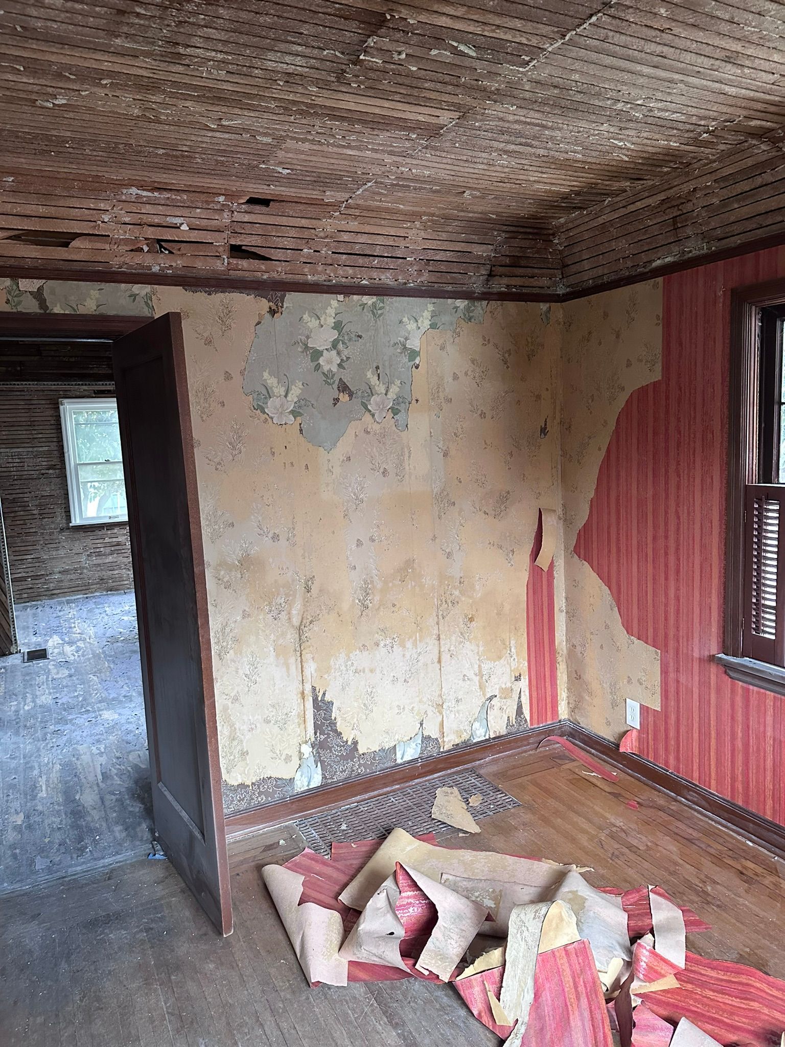 A room in an old house with peeling wallpaper and a window.