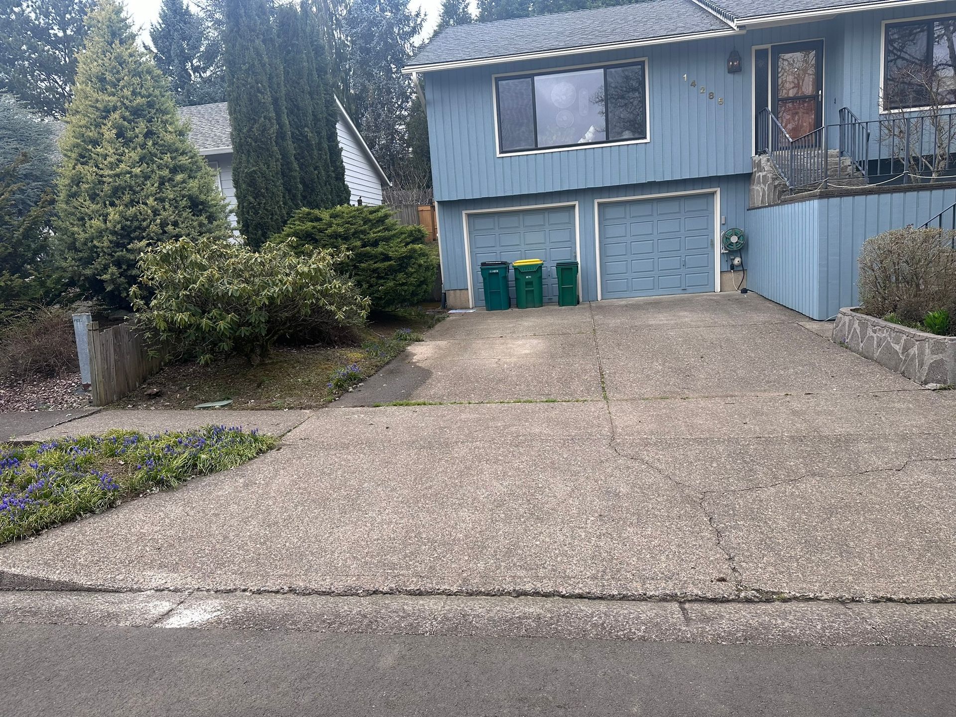 A blue house with a driveway and trash cans in front of it