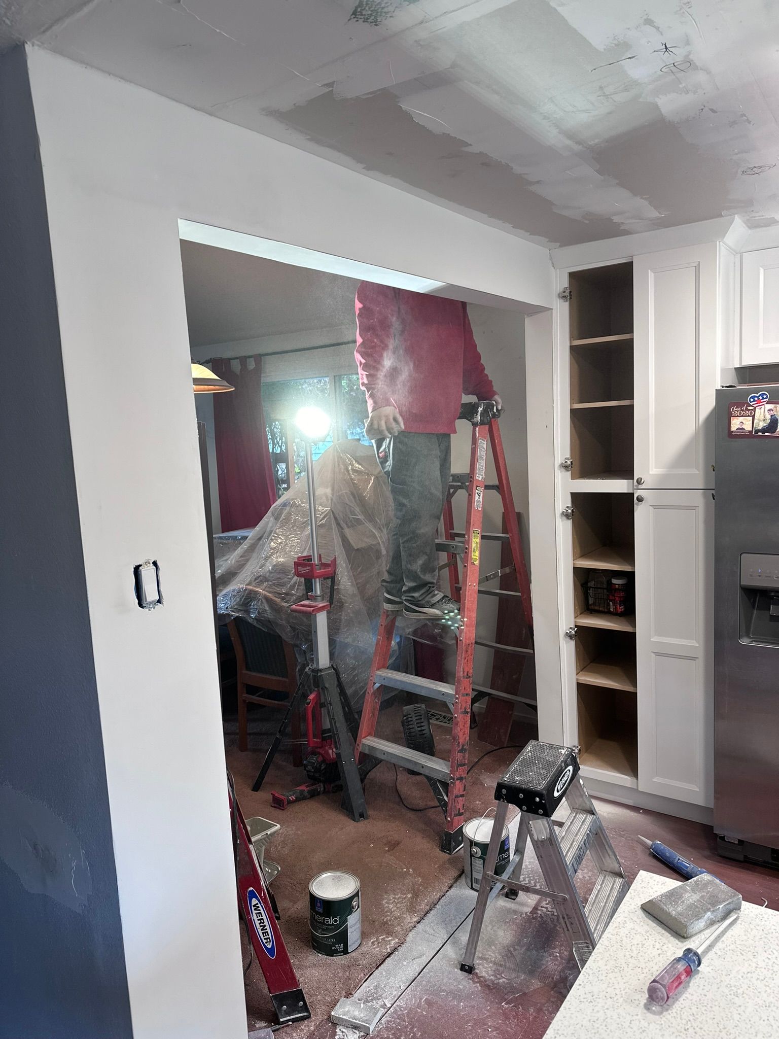 A person is standing on a ladder in a kitchen.