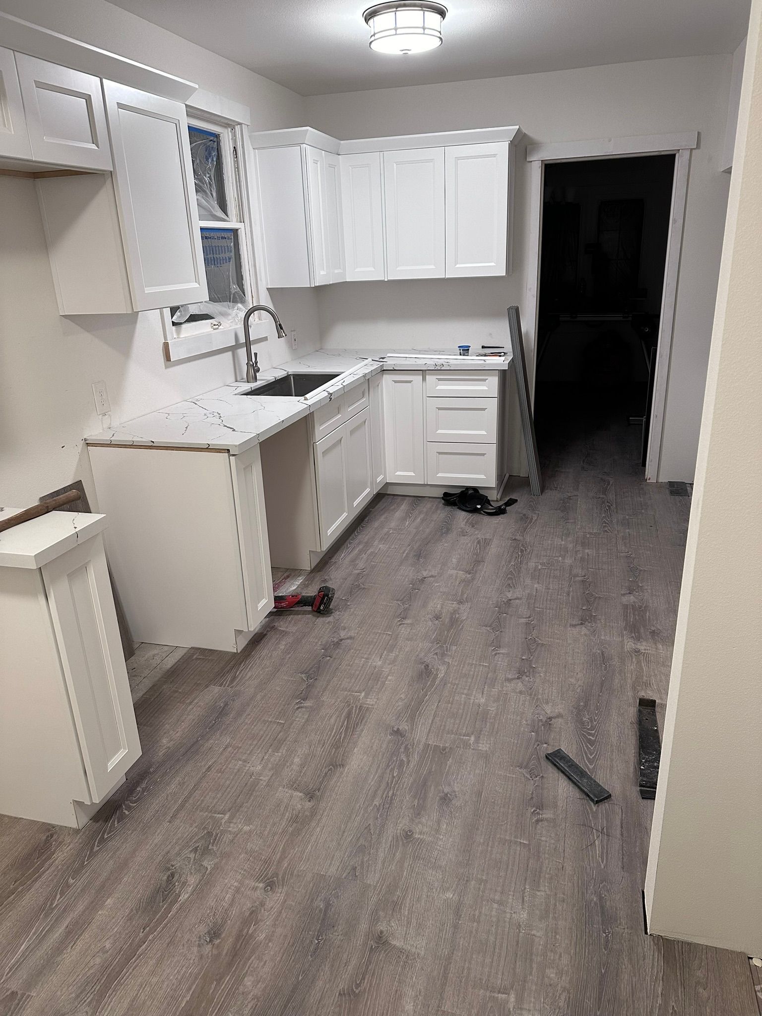 A kitchen with white cabinets , a sink , and a wooden floor.