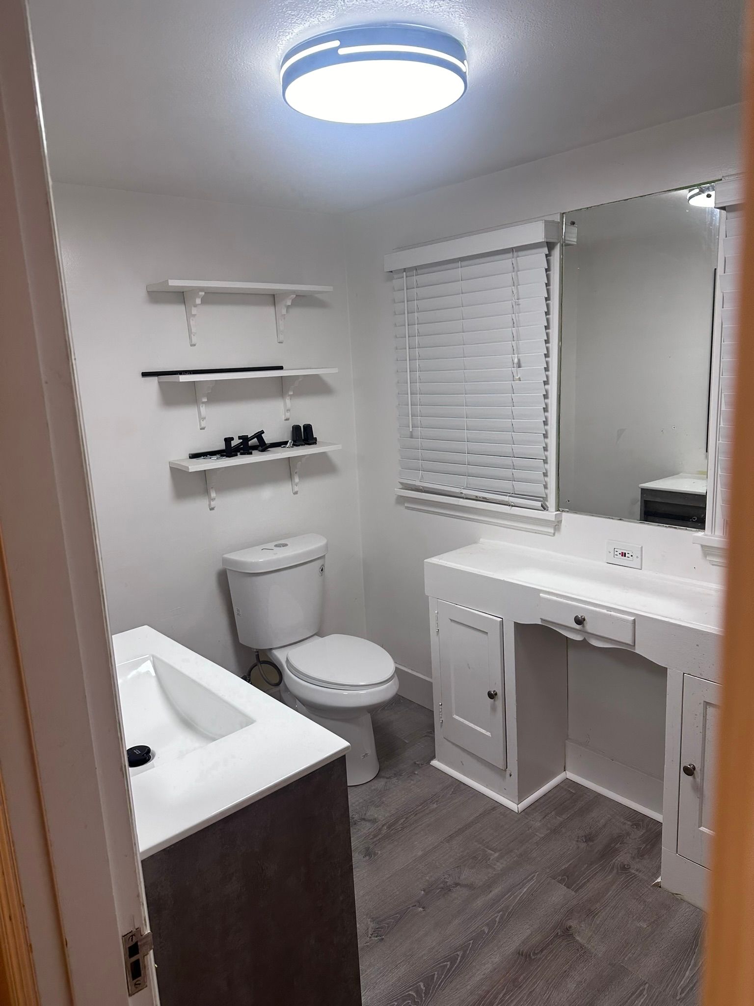 A bathroom with a toilet , sink , mirror and window.