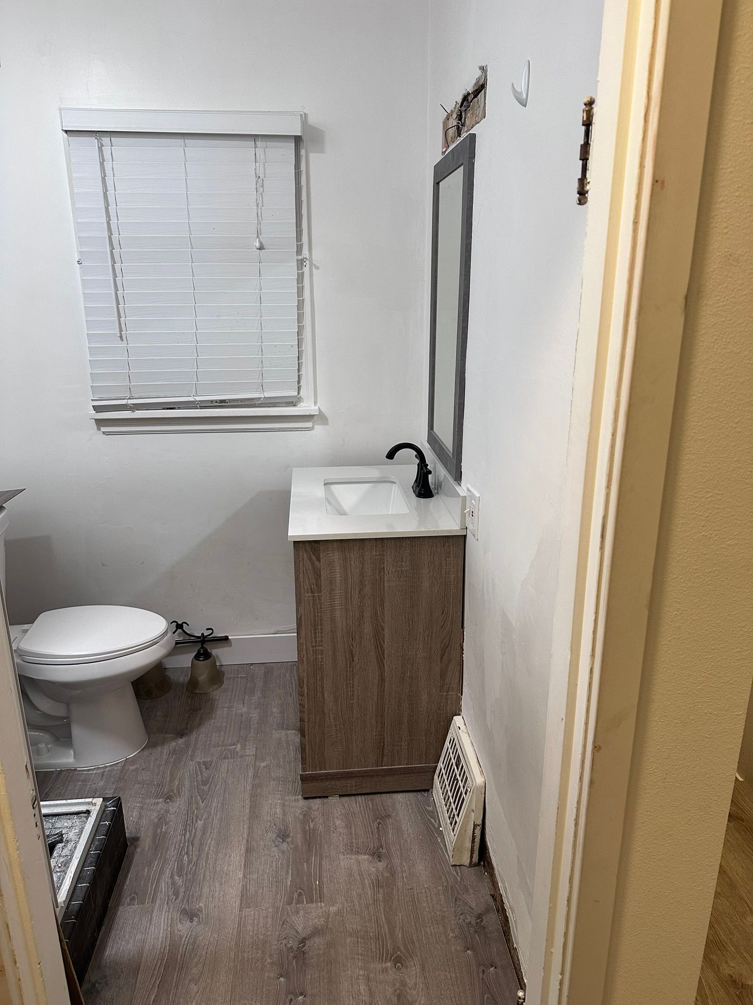 A bathroom with a toilet , sink , mirror and window.