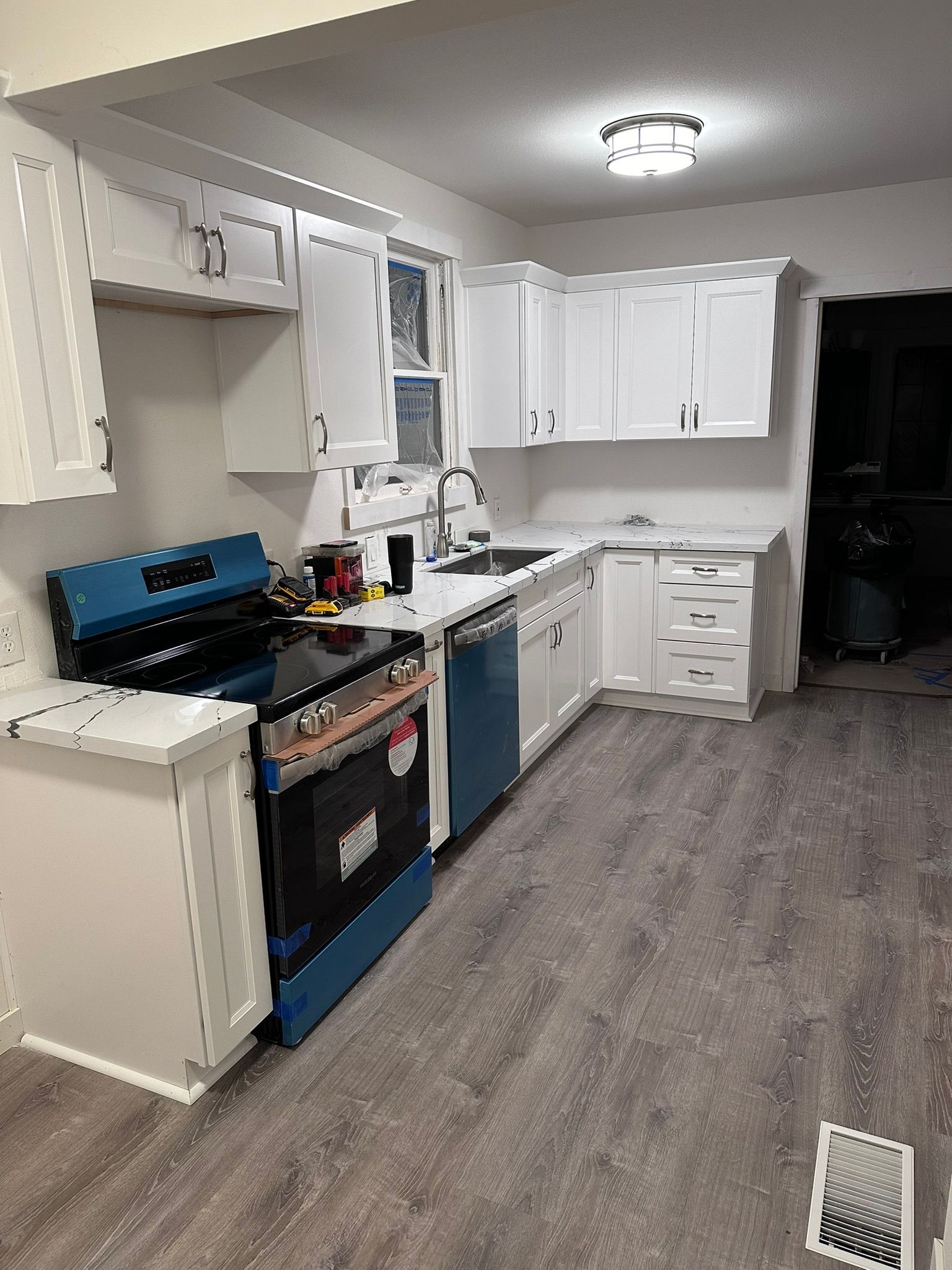 A kitchen with white cabinets , blue appliances , a stove and a sink.