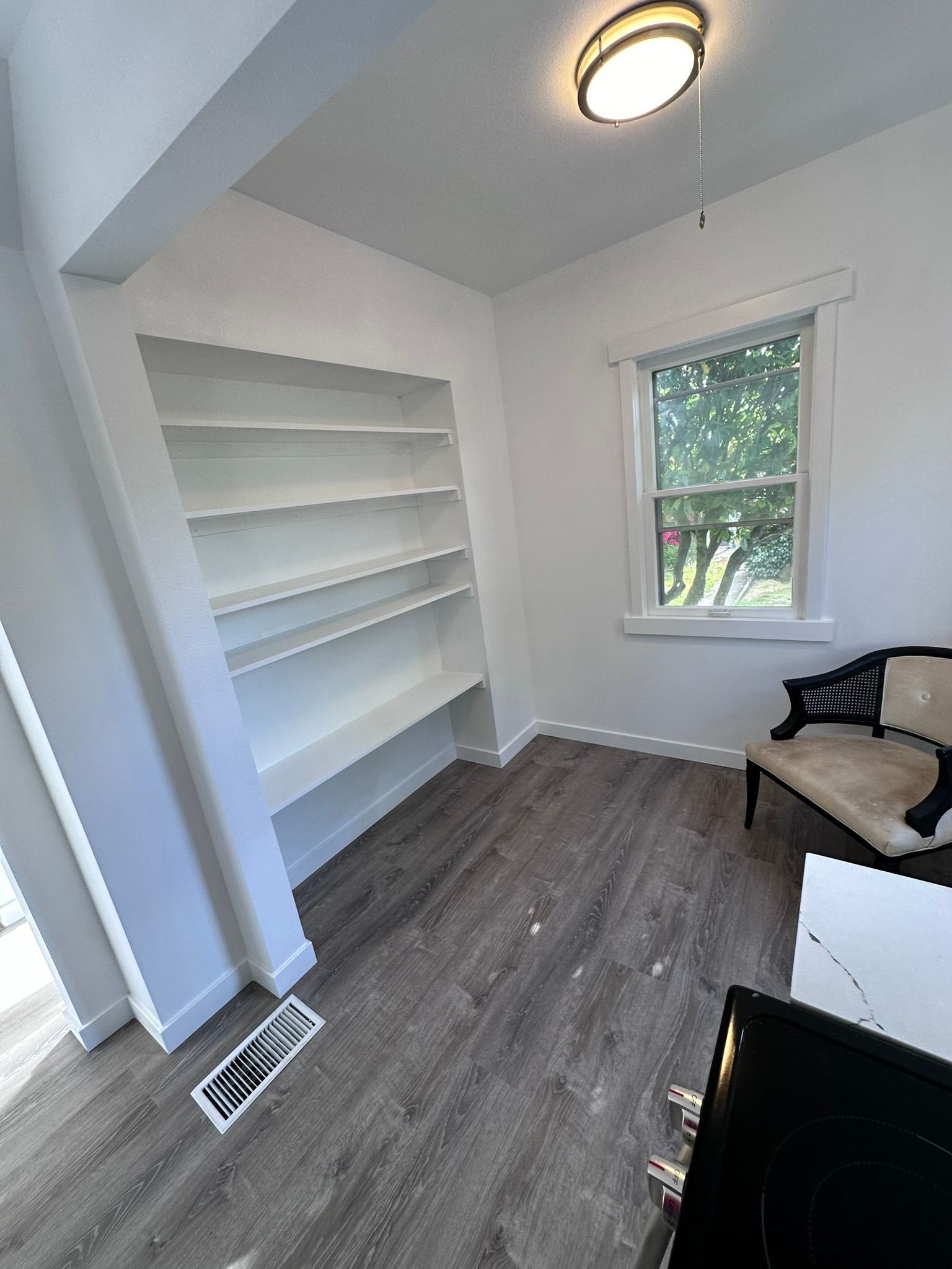 A living room with a bookshelf , chair , and window.
