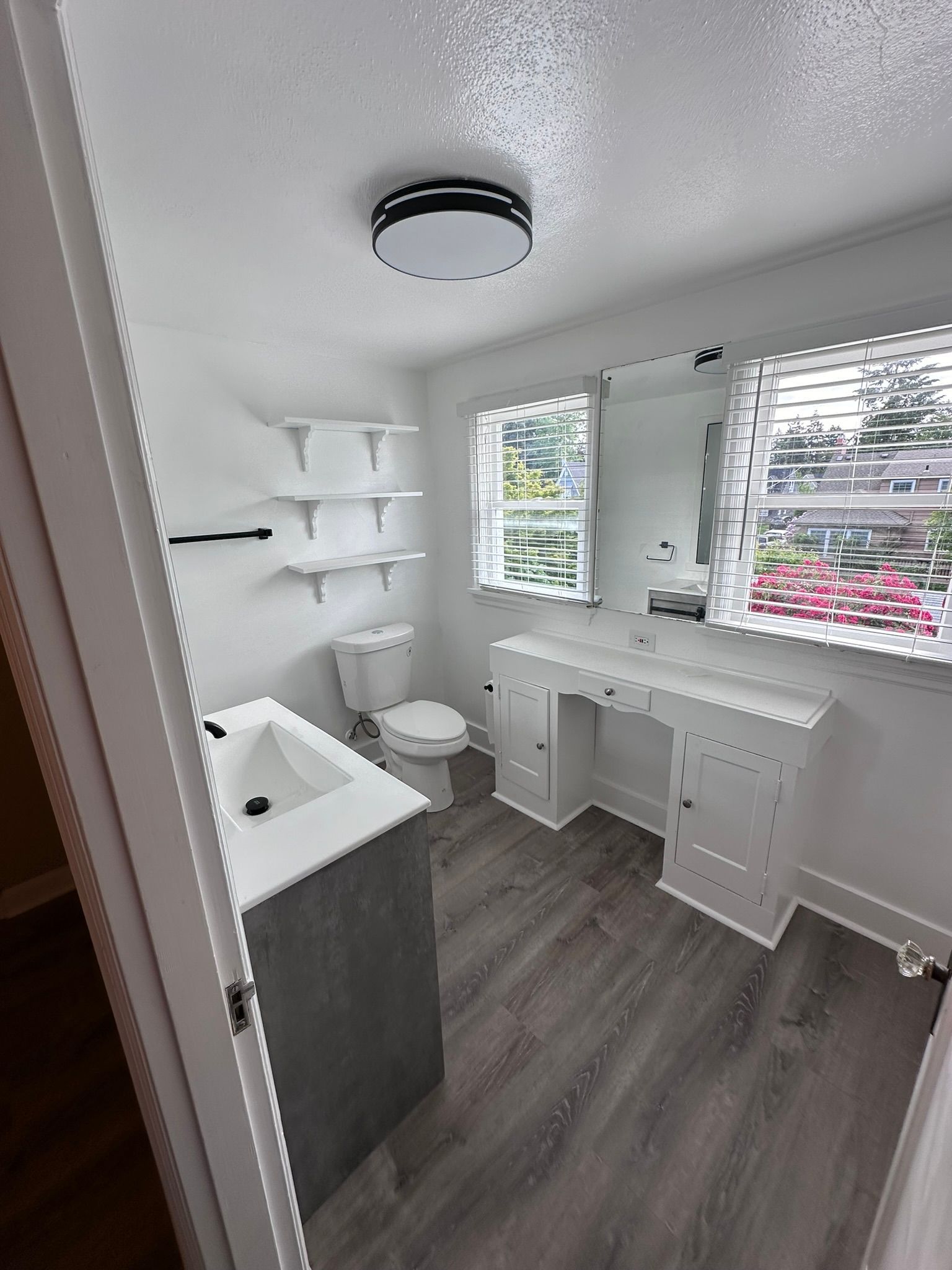 A bathroom with a toilet , sink , mirror and window.
