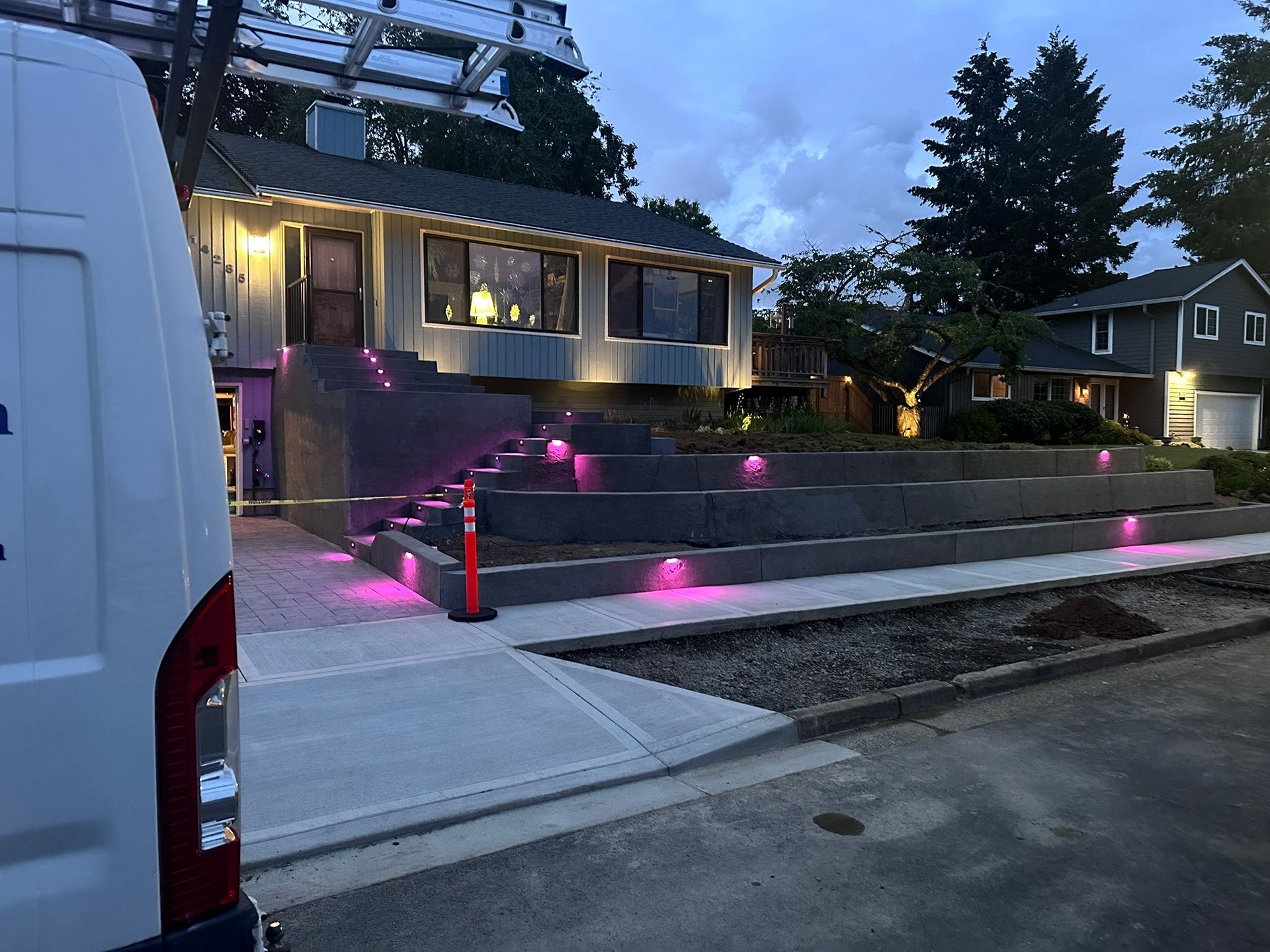 A white van is parked in front of a house with pink lights on the steps.
