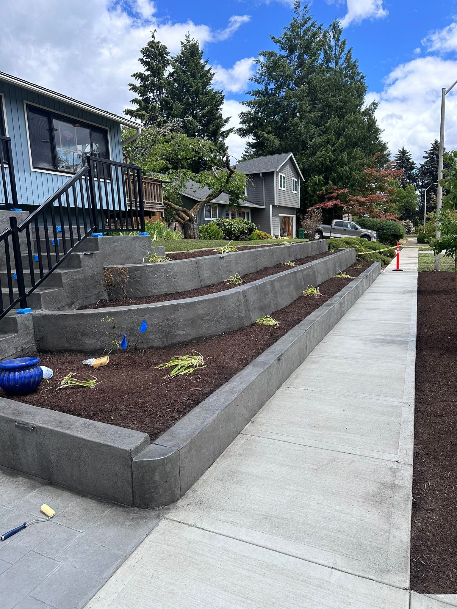 A sidewalk leading to a house with a staircase and a garden in front of it.