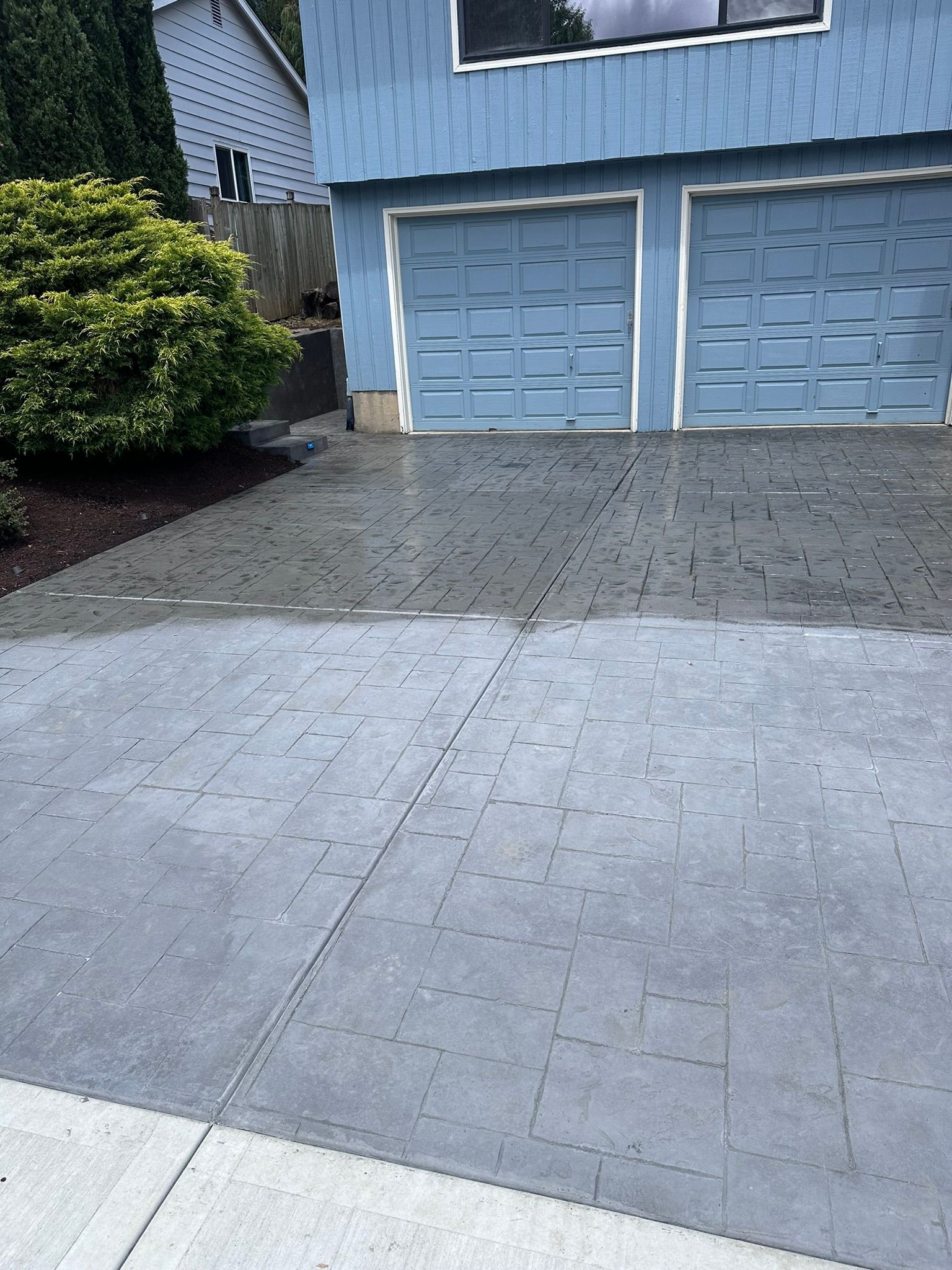 A driveway in front of a blue house with two garage doors