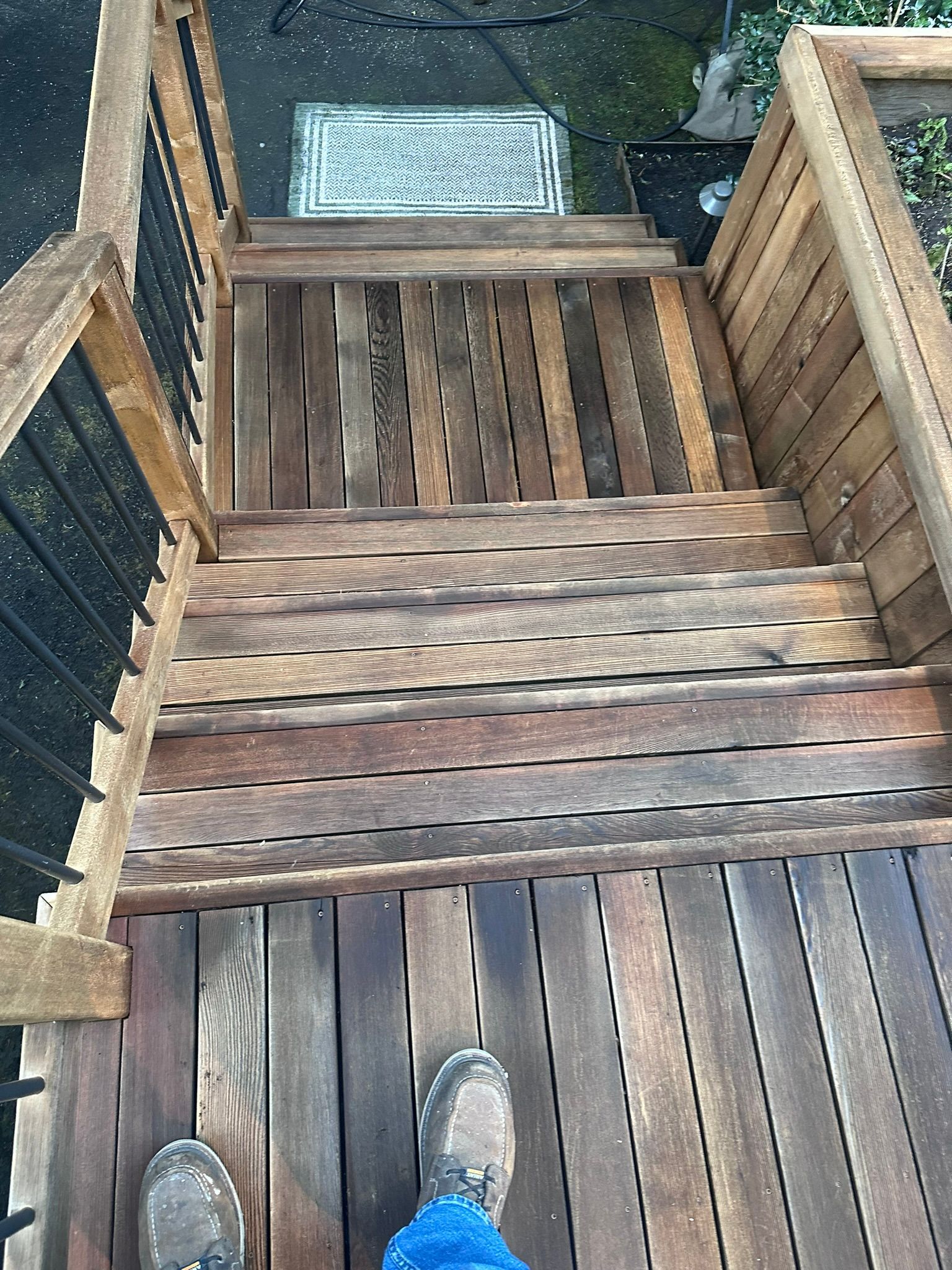 A person is standing on a wooden deck next to a wooden staircase.