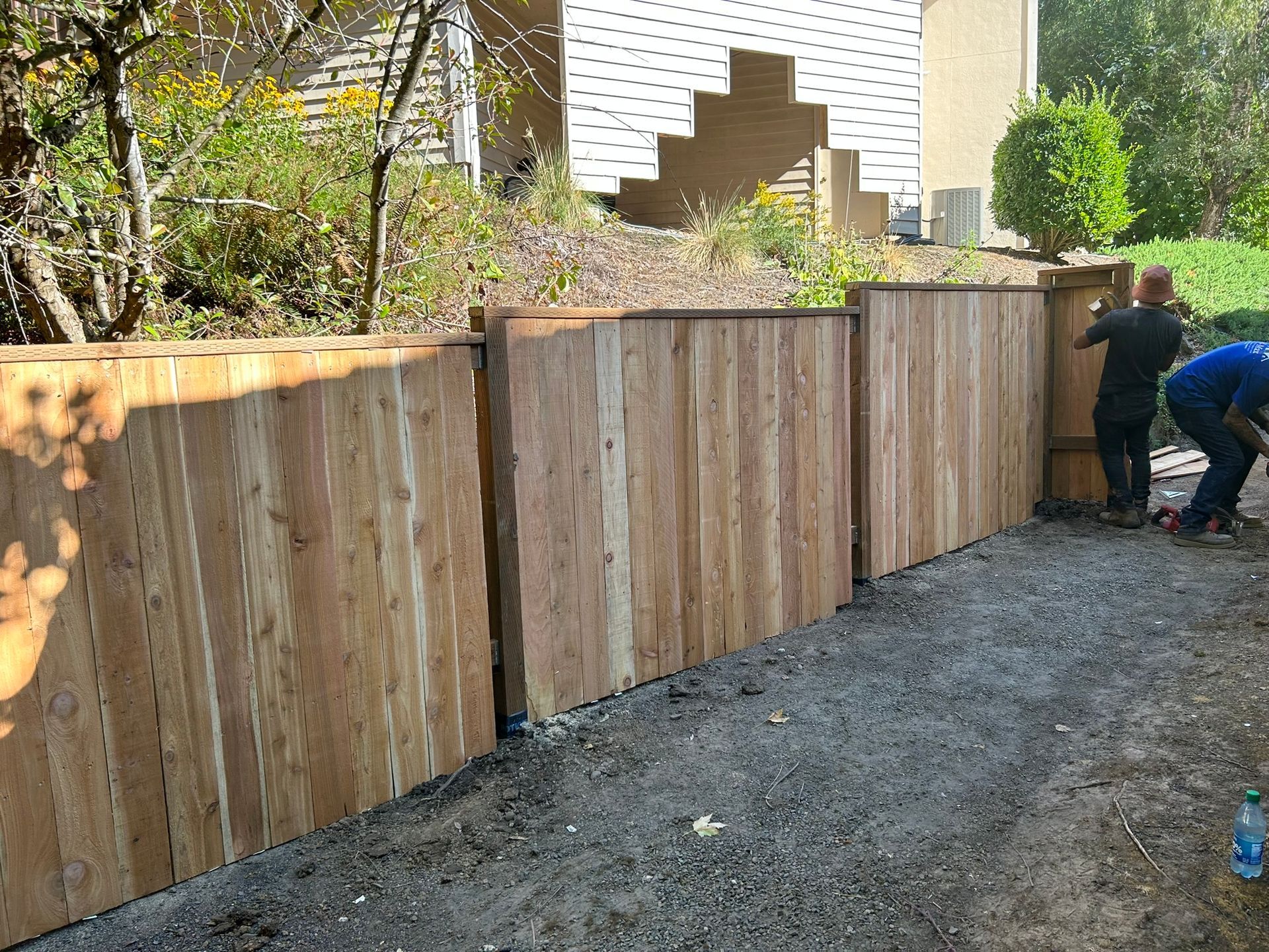 Two men are working on a wooden fence in front of a house.