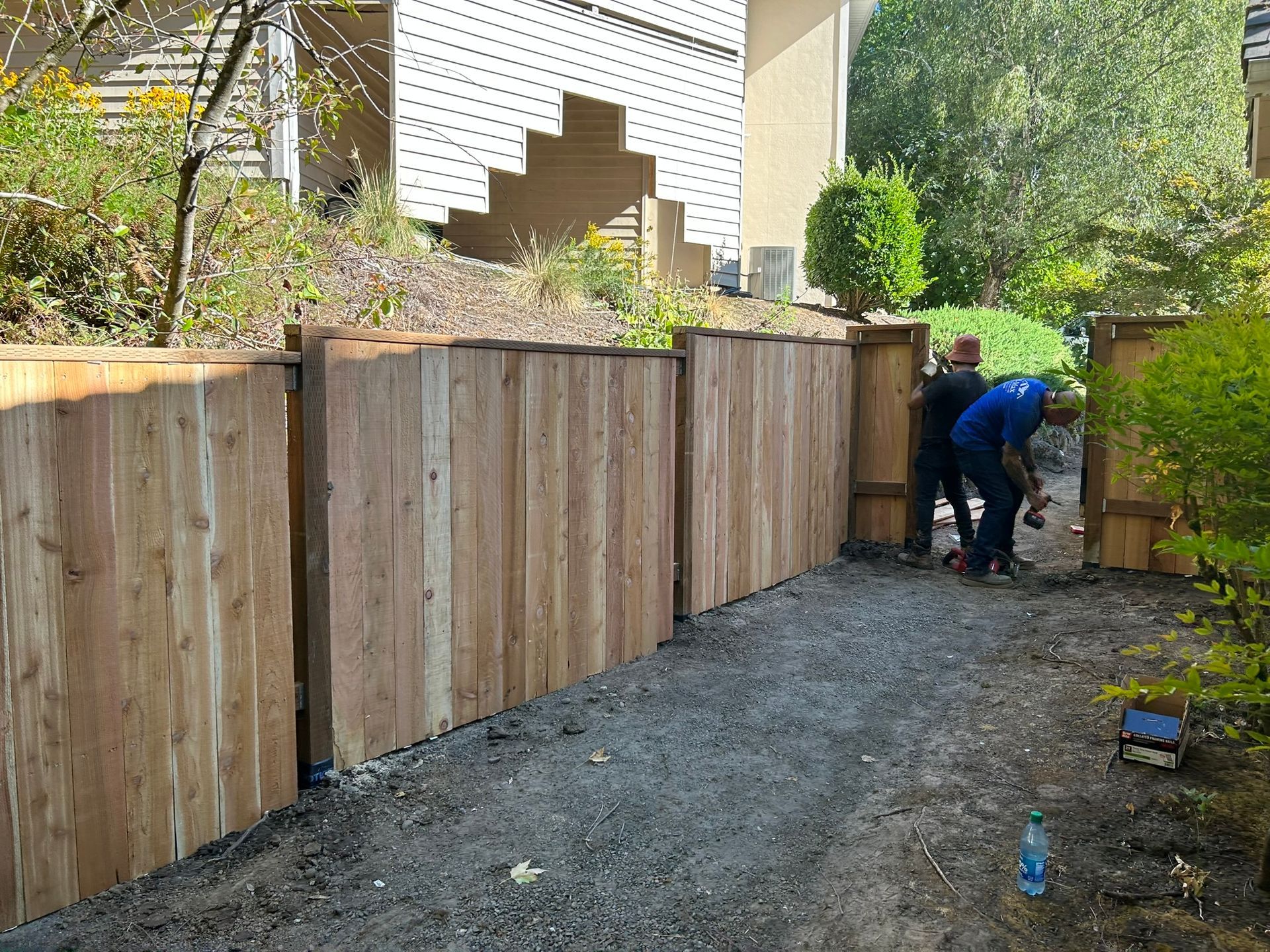 Two men are working on a wooden fence in front of a house.