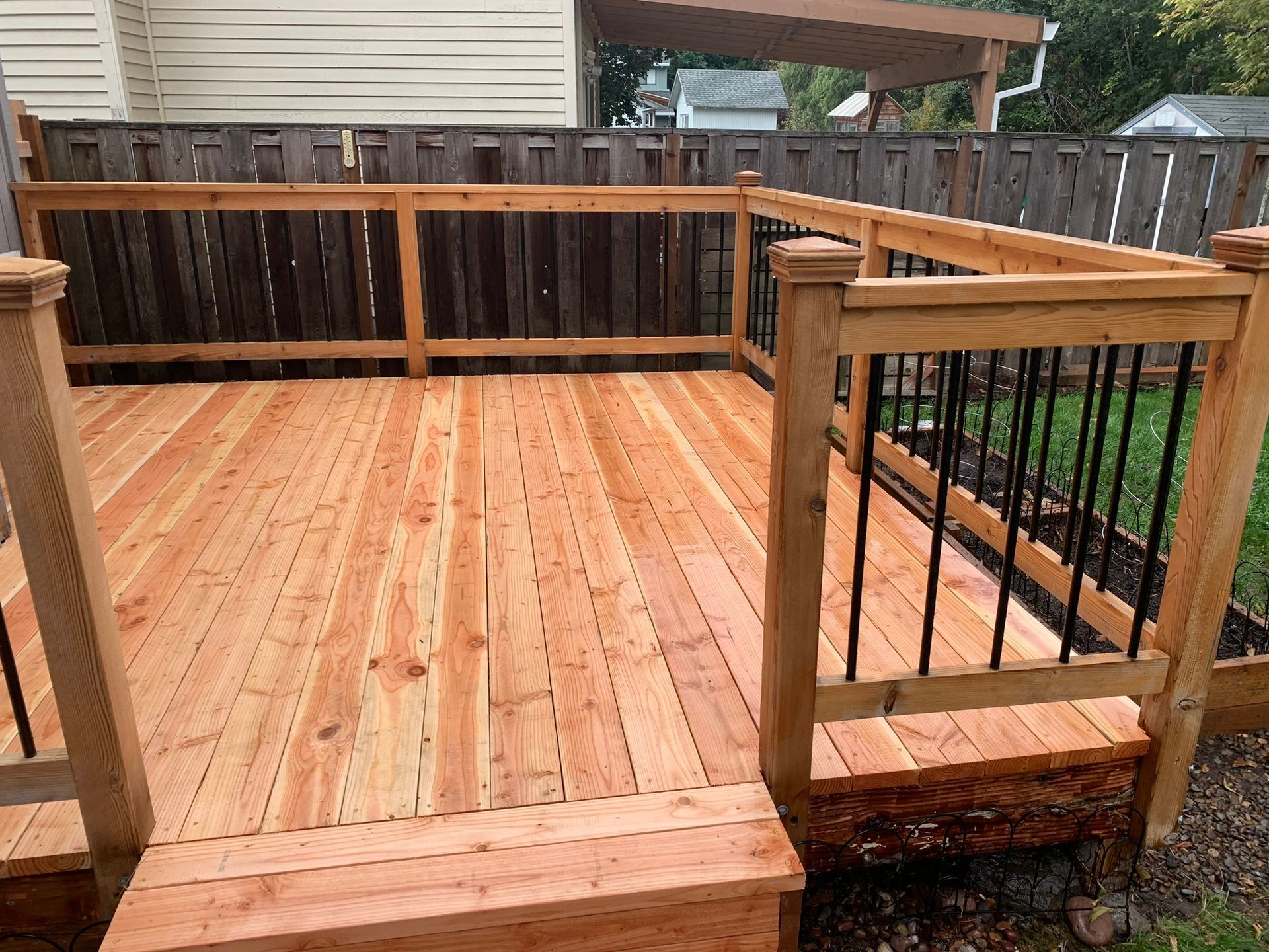 A wooden deck with stairs and a metal railing in a backyard.