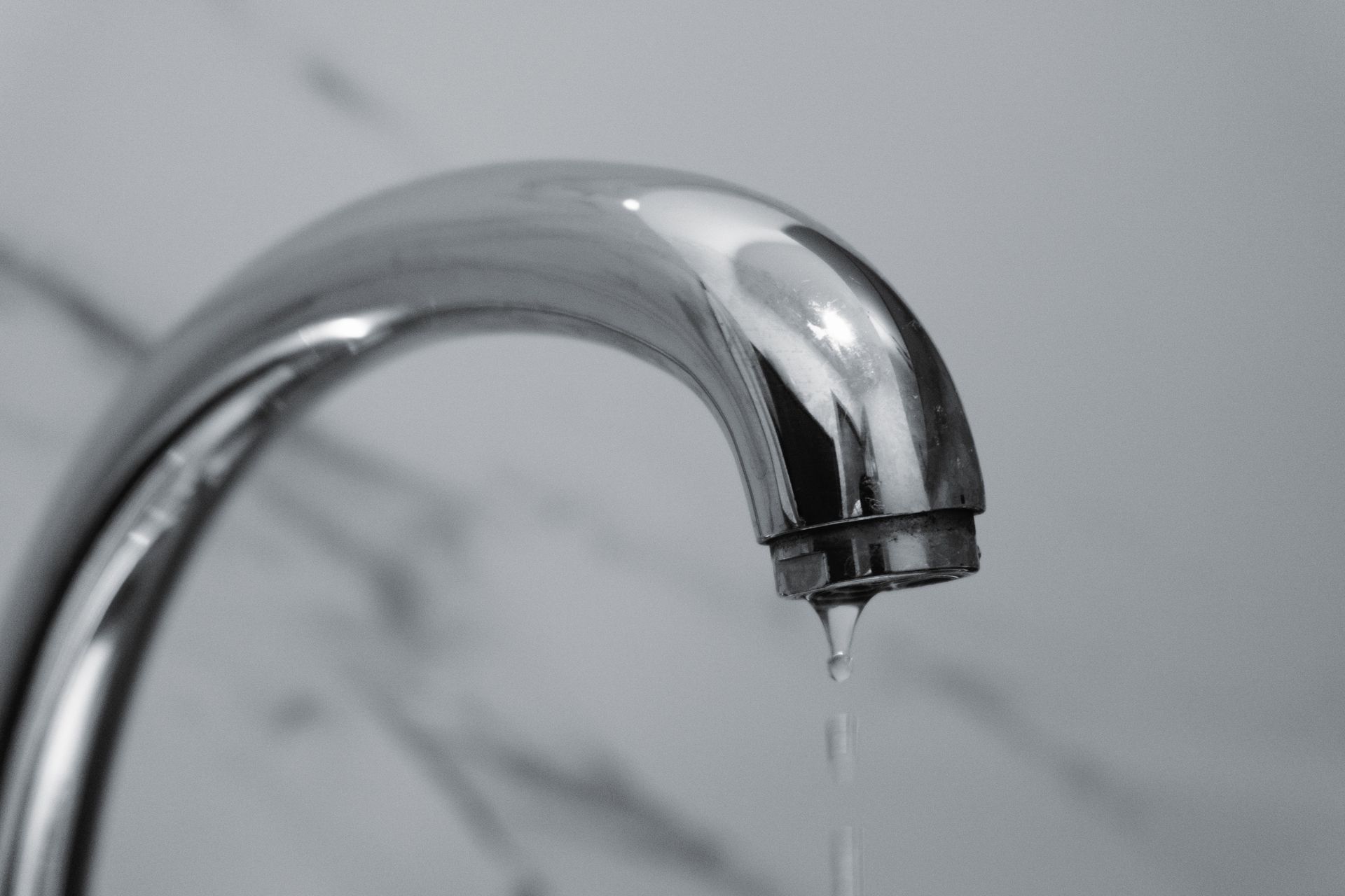 Close-up of a chrome faucet dripping water over a sink.