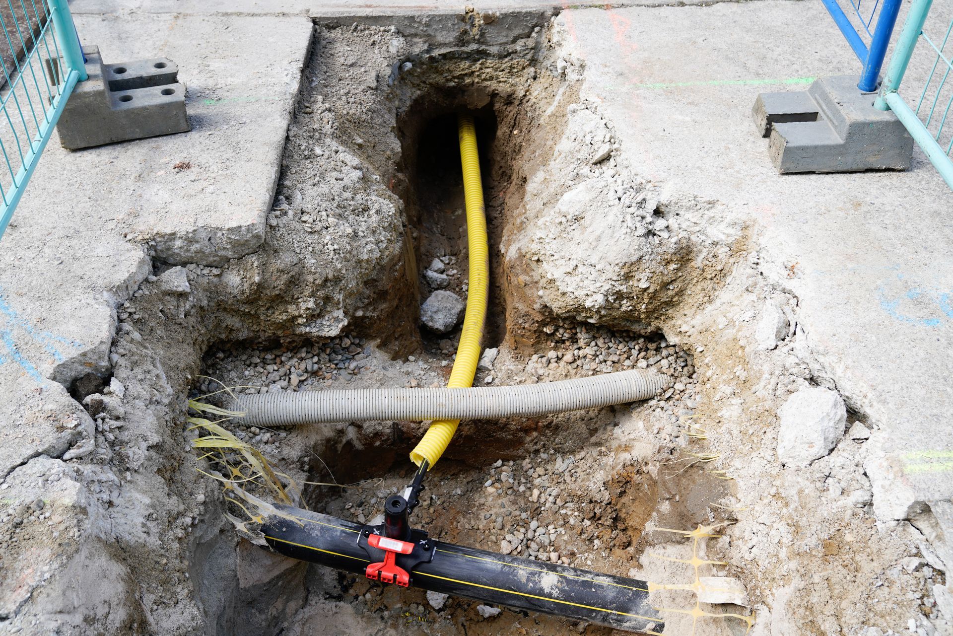 Damaged concrete around exposed yellow cable and pipe at a construction trench opening