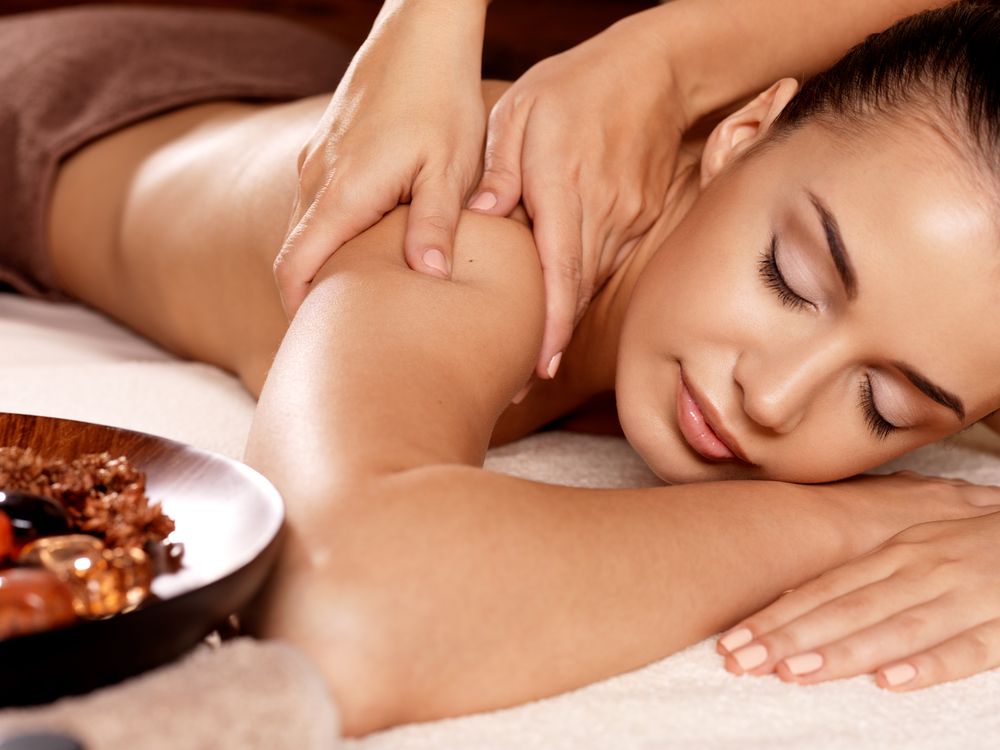 Woman Receiving a Relaxing Shoulder Massage with Stones and Candles Nearby — Hope Laser and Beauty Clinic In Taree, NSW
