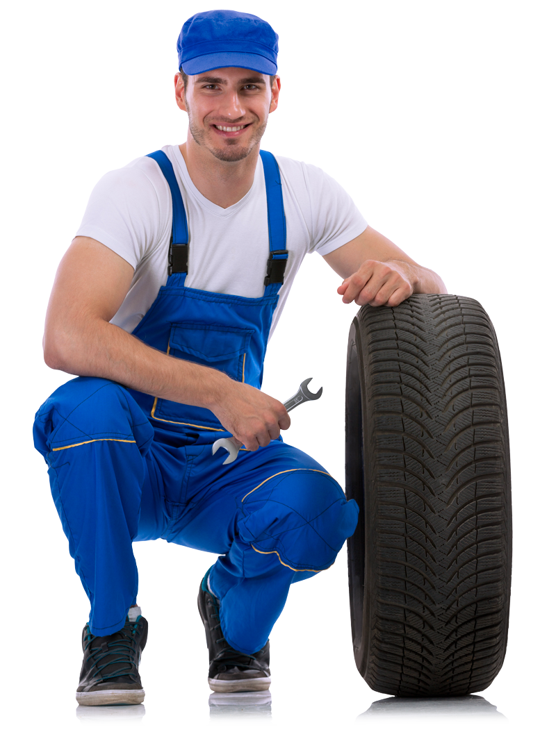 A Man in Blue Overalls Is Kneeling Next to A Tire and Holding a Wrench.