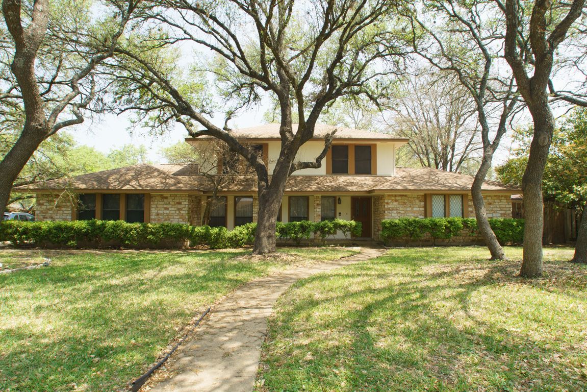 Two-story brick house with large trees, lawn, and walkway.