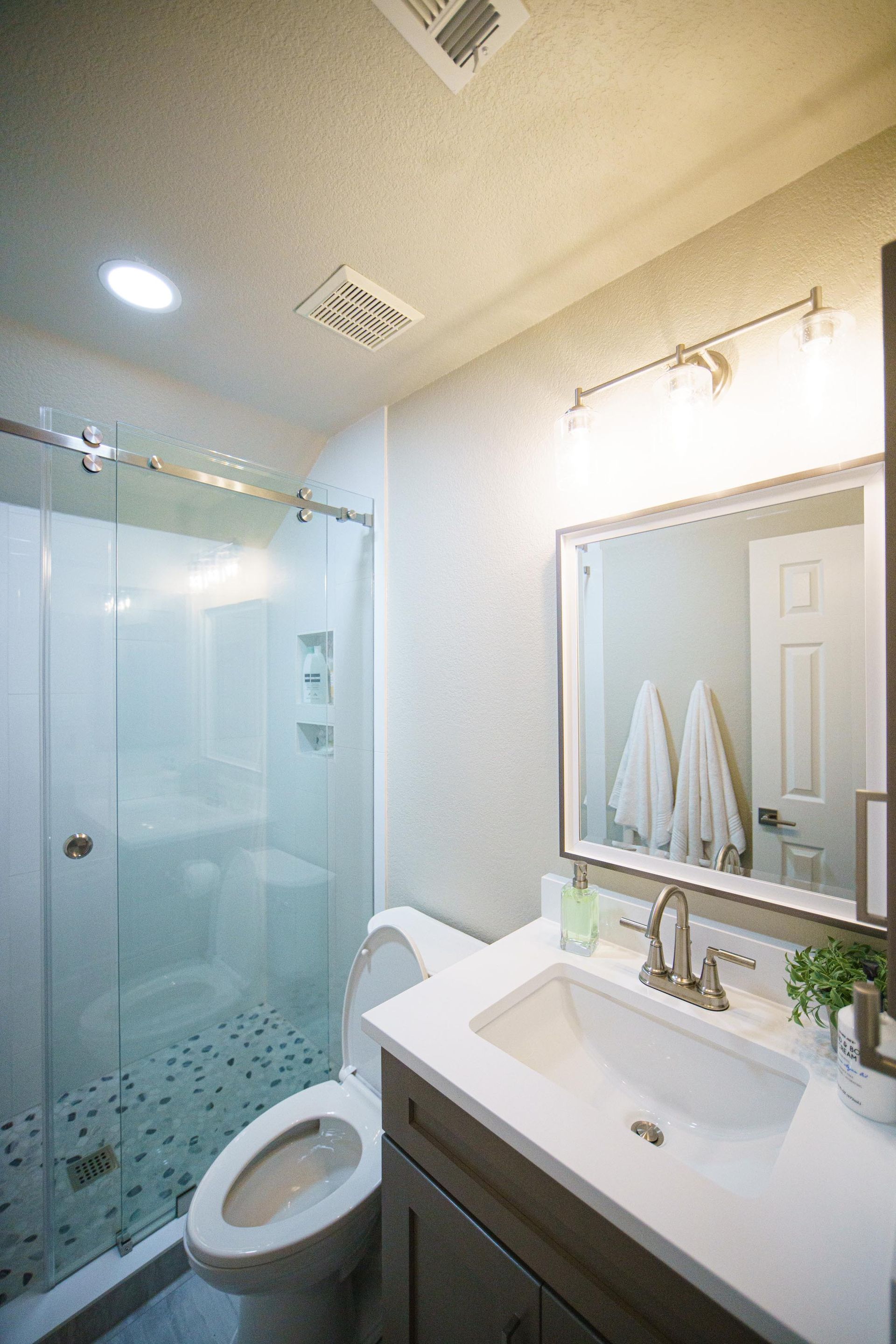 Bathroom with a glass shower, toilet, vanity with mirror, and white towels.
