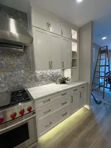 Modern kitchen with white cabinets, stainless steel range hood, marble backsplash, and under-cabinet lighting.