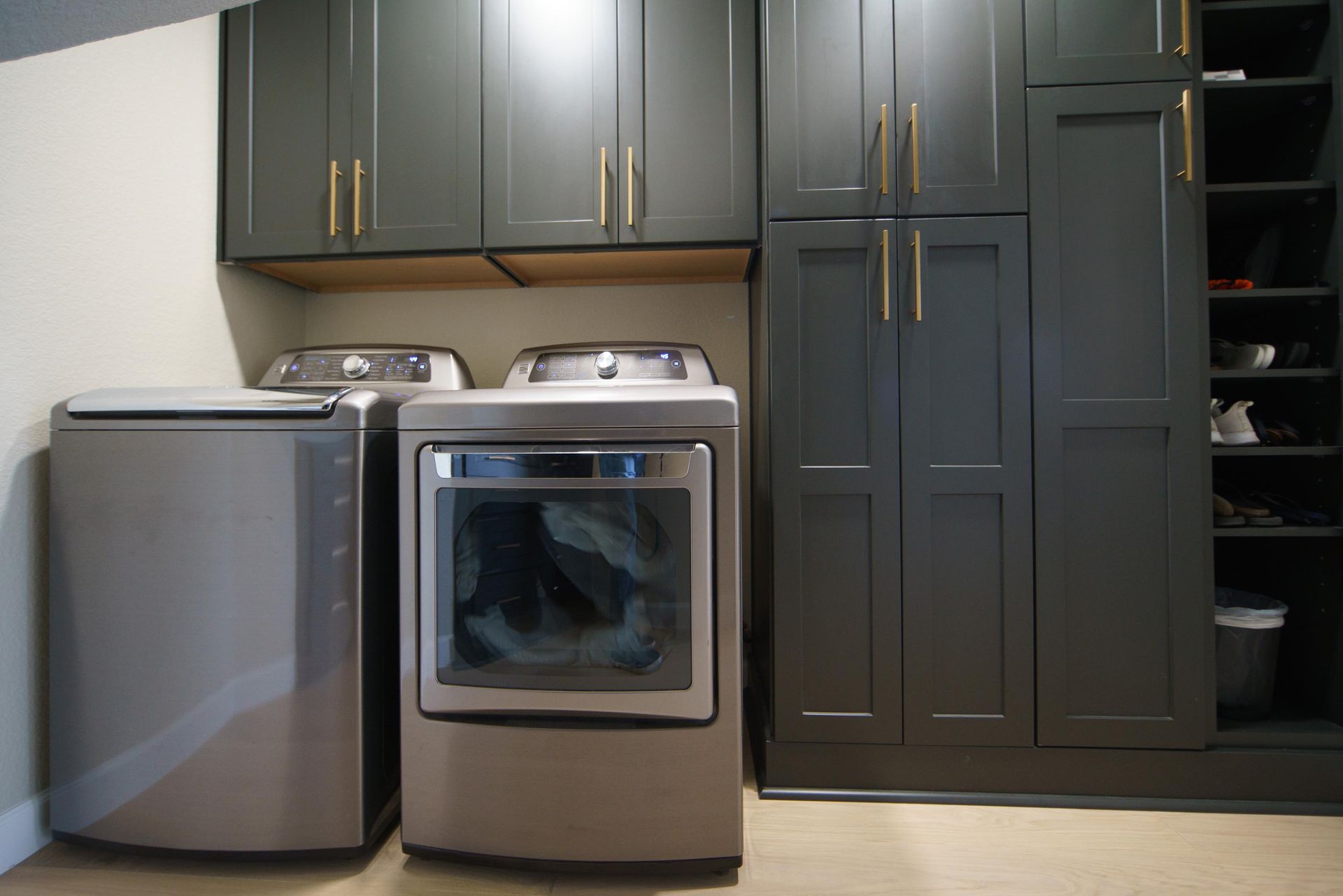 Laundry room with gray cabinets, washer, dryer, and storage shelves.