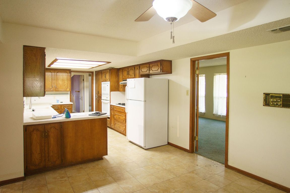 Kitchen with wooden cabinets, white appliances, and a doorway to a living room.