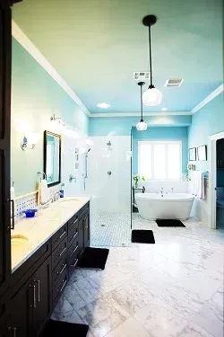 Spacious, light blue bathroom with white marble floors, a glass shower, and a freestanding tub.