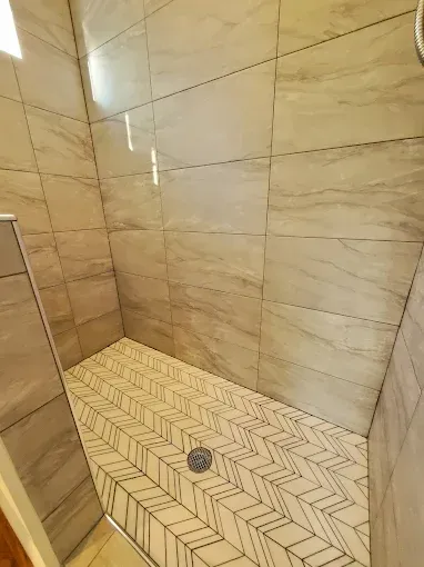 Tiled shower with gray walls and a patterned floor, angled design.