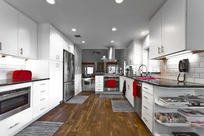 Modern, white kitchen with stainless steel appliances and dark wood floors.