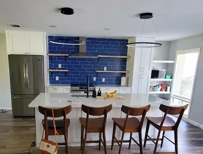Modern kitchen with a blue tiled backsplash, white island, and wooden bar stools.
