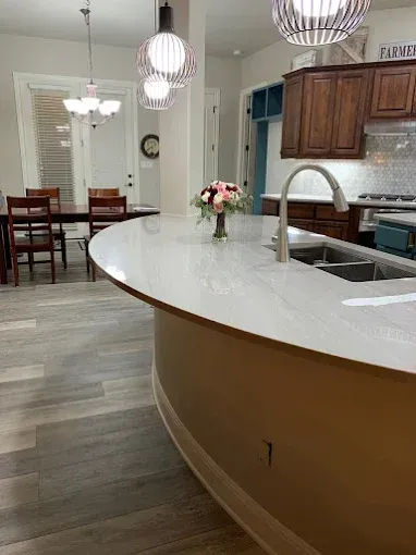 Kitchen with a curved white countertop, brown cabinets, and a dining area visible.
