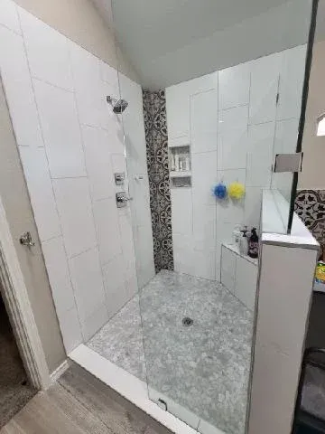 Modern shower with white tiled walls, glass doors, and gray stone floor.