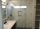Bathroom with marble-like tiled shower and wall, white countertop, black fixtures, and built-in shelves.