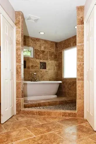 Bathroom with a raised bathtub area tiled in brown, flanked by two white doors.