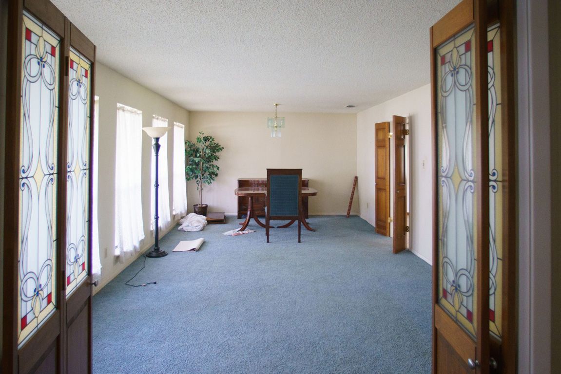 Empty room with teal carpet, stained glass doors, and a desk.