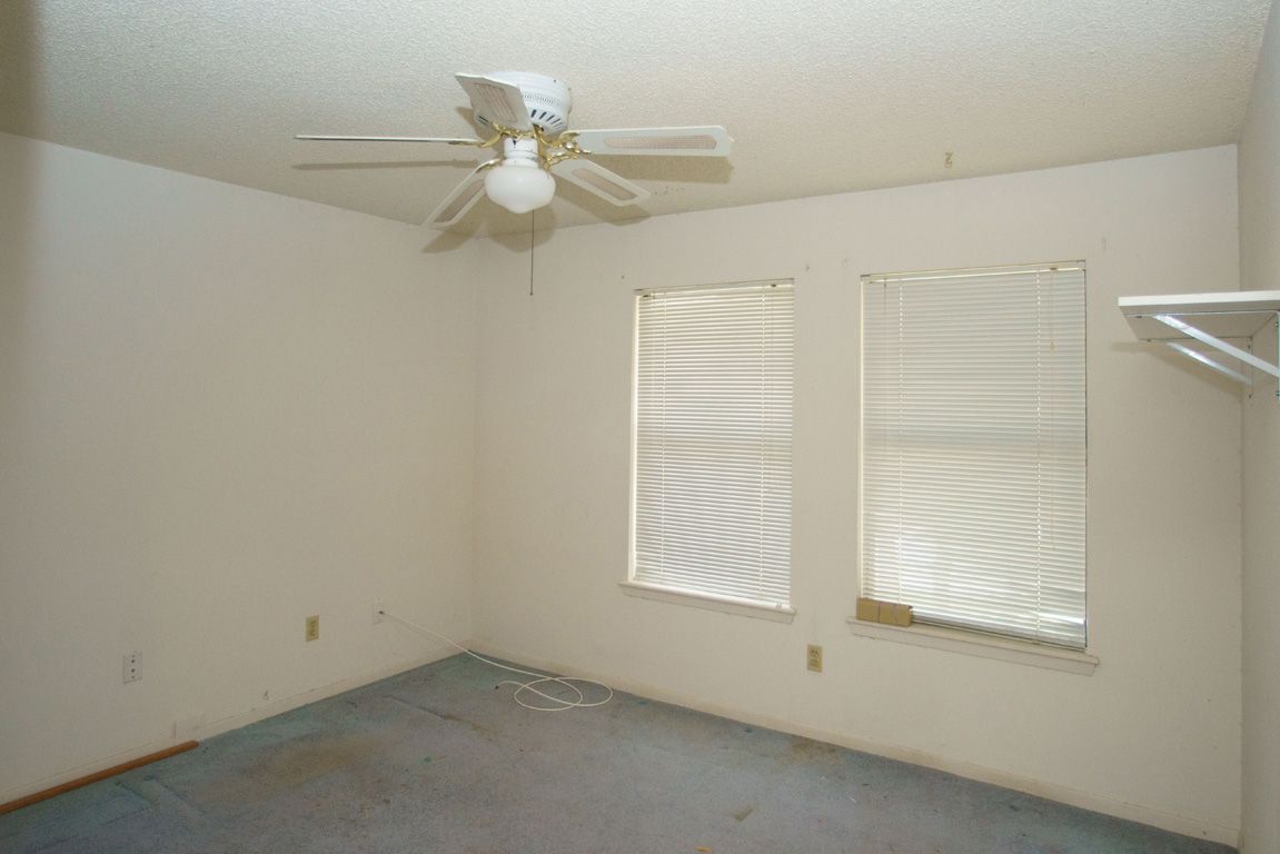 Empty room with blue carpet, two windows with blinds, ceiling fan, and white walls.