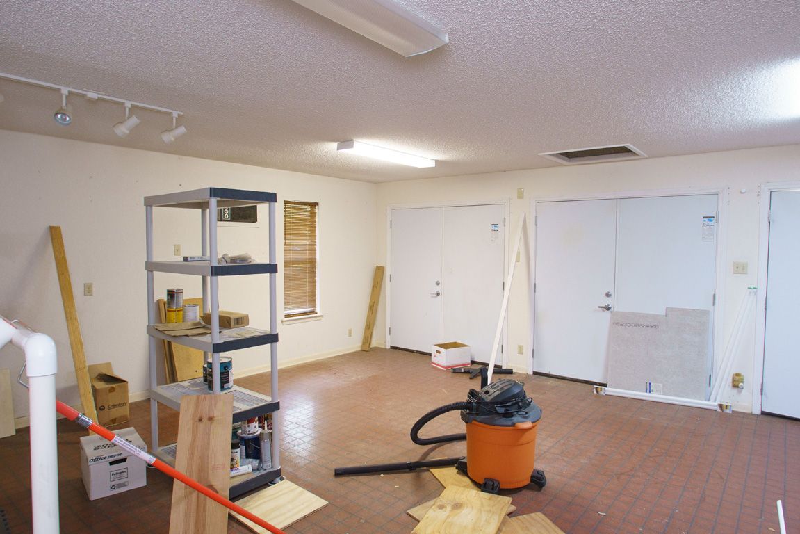 Empty room with shelving unit, vacuum, and doors. Brown flooring and white walls.