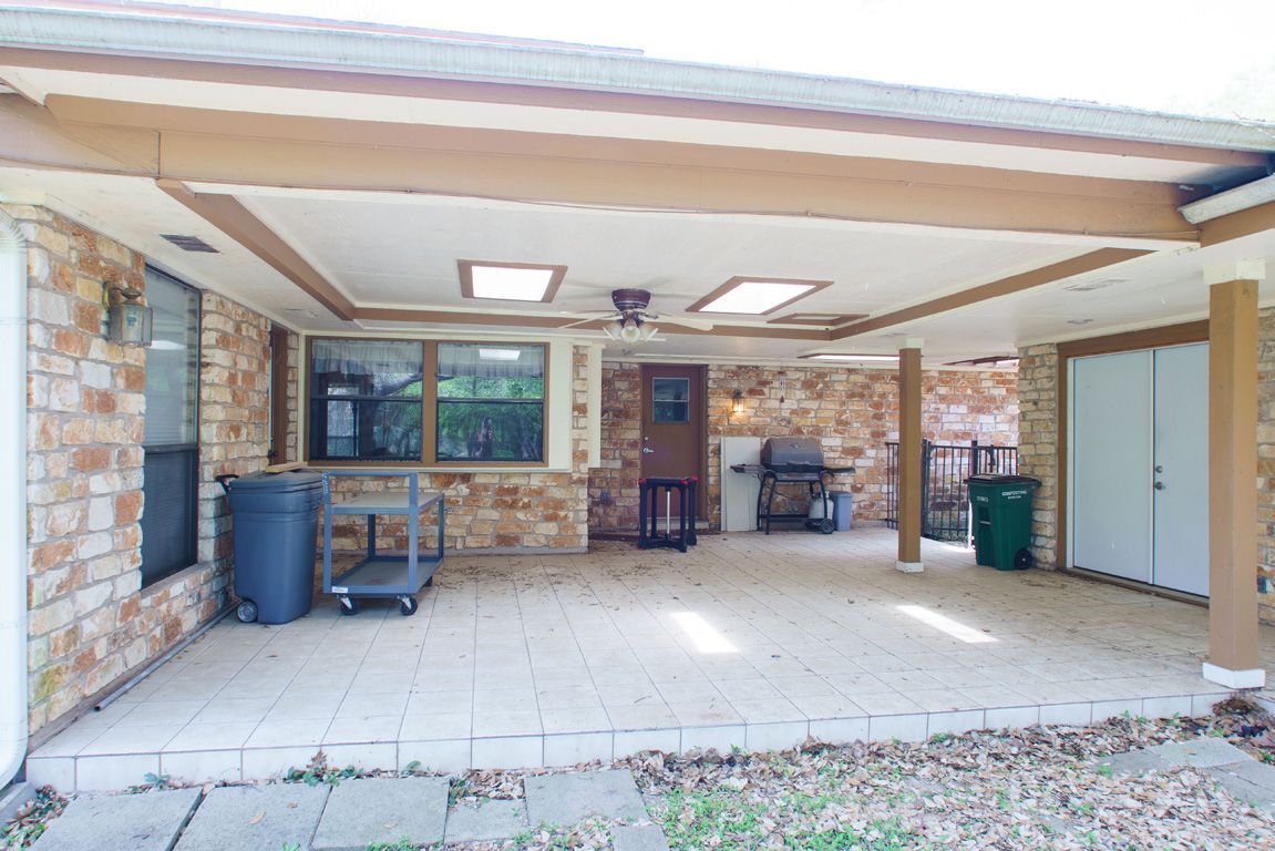 Covered patio with brick walls and stone flooring, featuring a grill and storage containers.