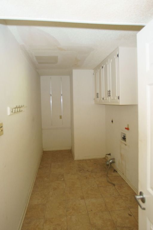 Empty laundry room with white cabinets and beige flooring.