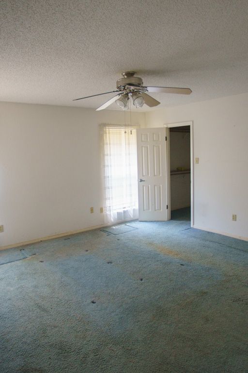 Empty room with teal carpet, white walls, ceiling fan, and partially open door to a bathroom.