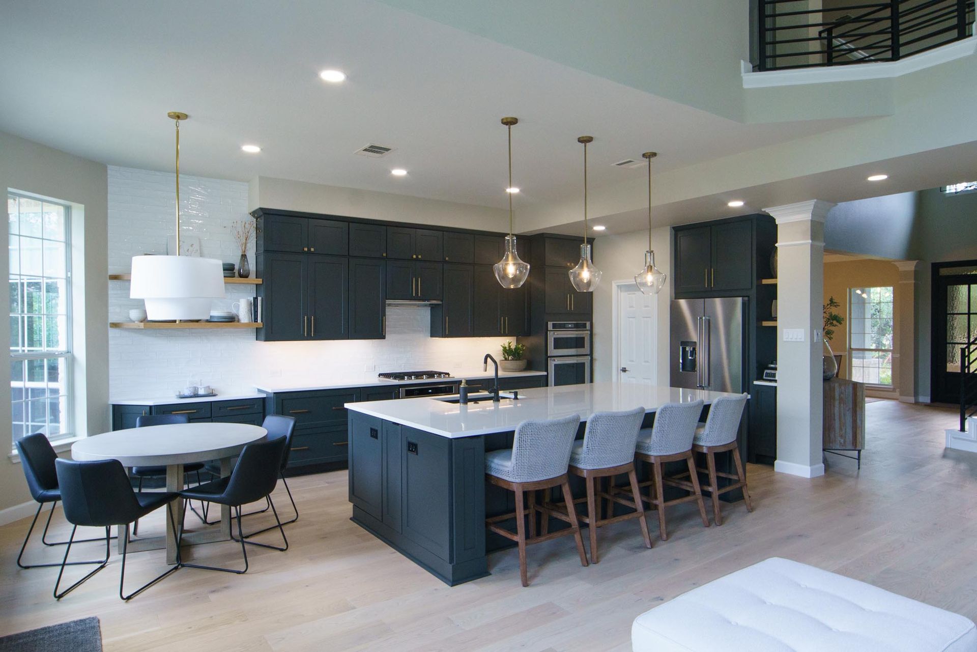 Modern kitchen with dark blue cabinets, large island, dining table, and light wood floors.