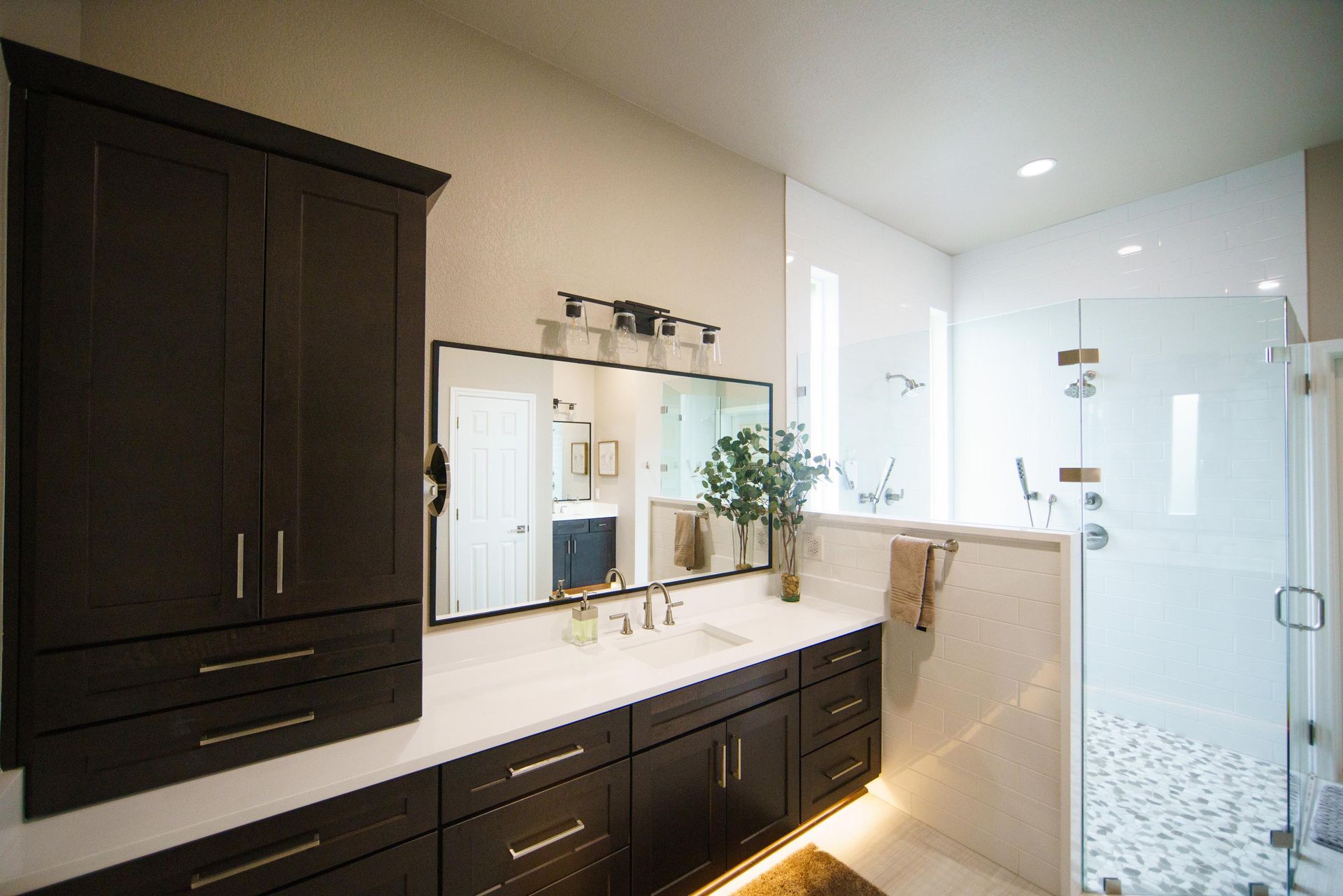 Modern bathroom with dark cabinets, white countertops, large mirror, and glass shower.