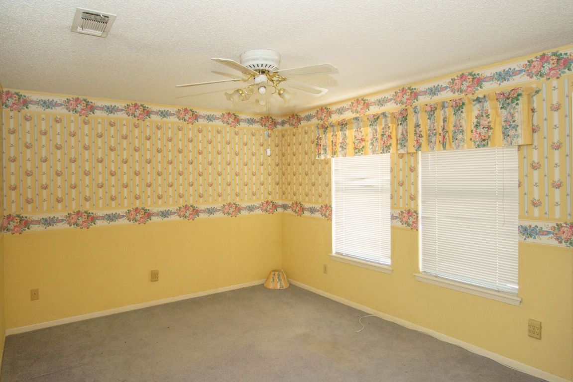 Yellow and floral wallpapered room with a ceiling fan, two windows with blinds, and gray carpet.