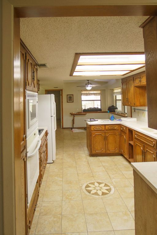 Kitchen with wood cabinets, white appliances, and tan tile floor.
