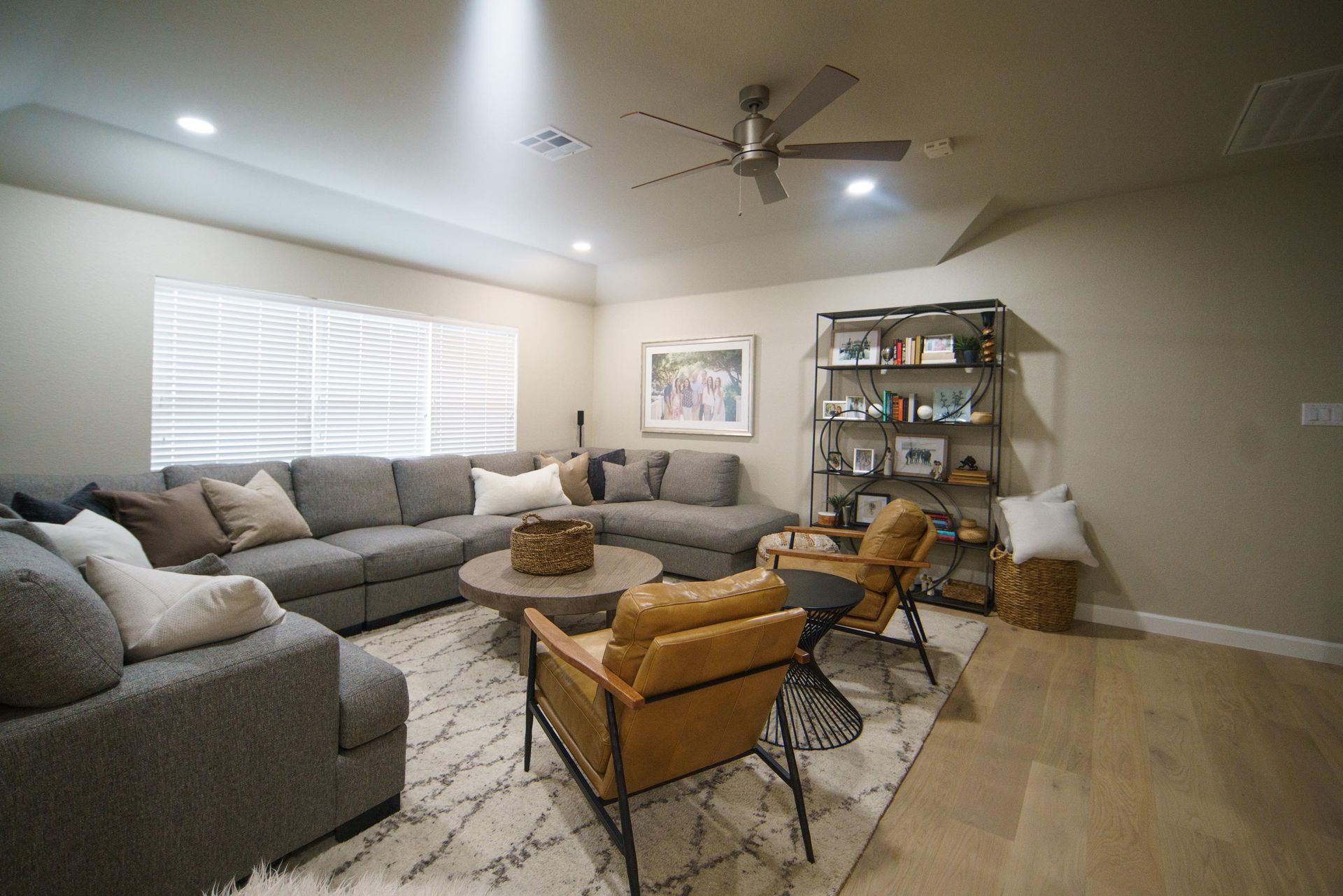 A modern living room with a sectional sofa, two tan armchairs, rug, and a bookshelf.