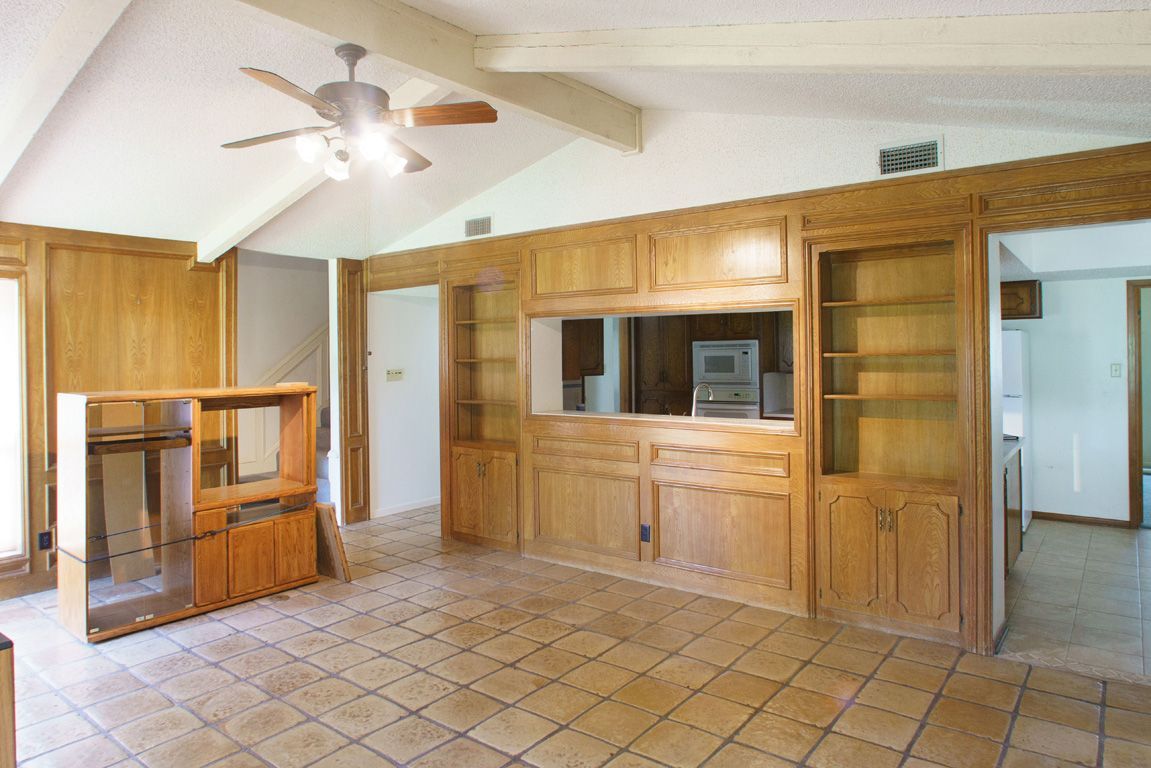 Empty room with wooden built-ins, open doorways, tile floor, and a ceiling fan.