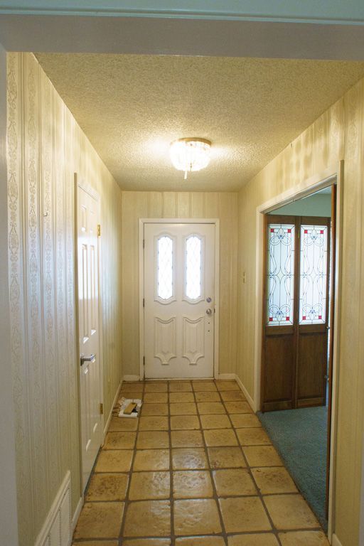 Hallway with white door, tile floor, and paneled walls. Doorway to room on the right.