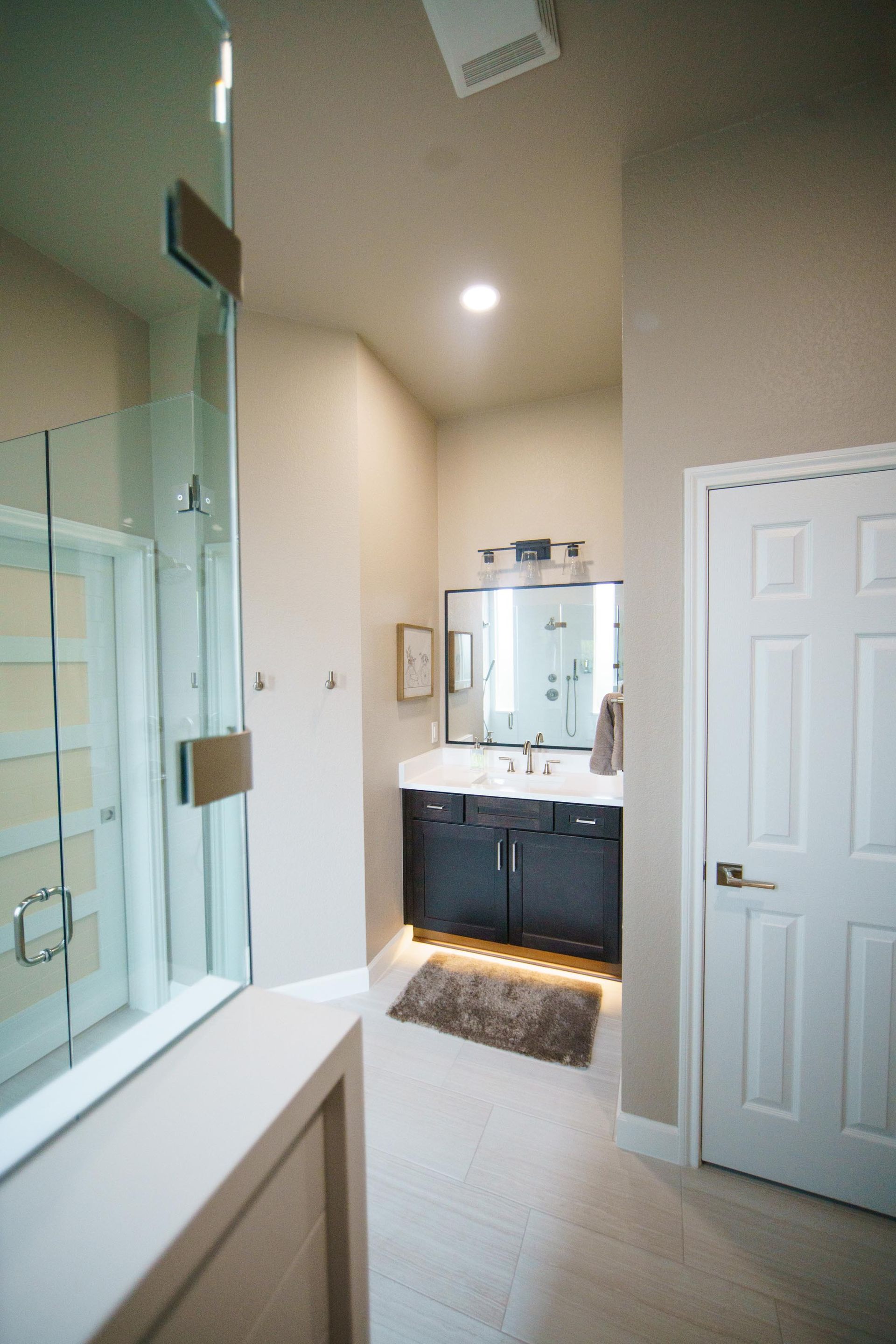 Bathroom interior with glass shower, vanity with mirror, and white door.