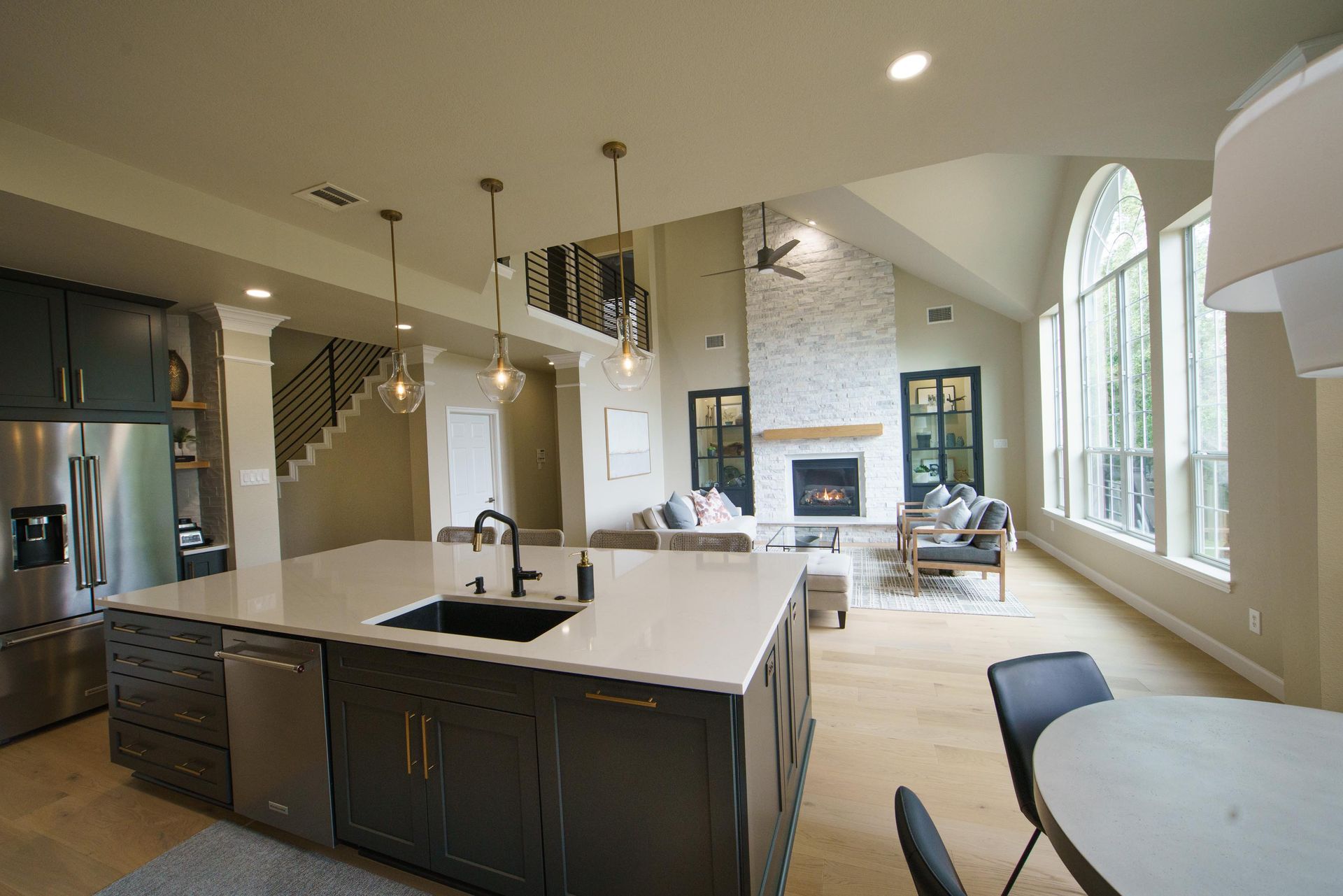 Open-concept kitchen with island, living area, fireplace, and large windows.