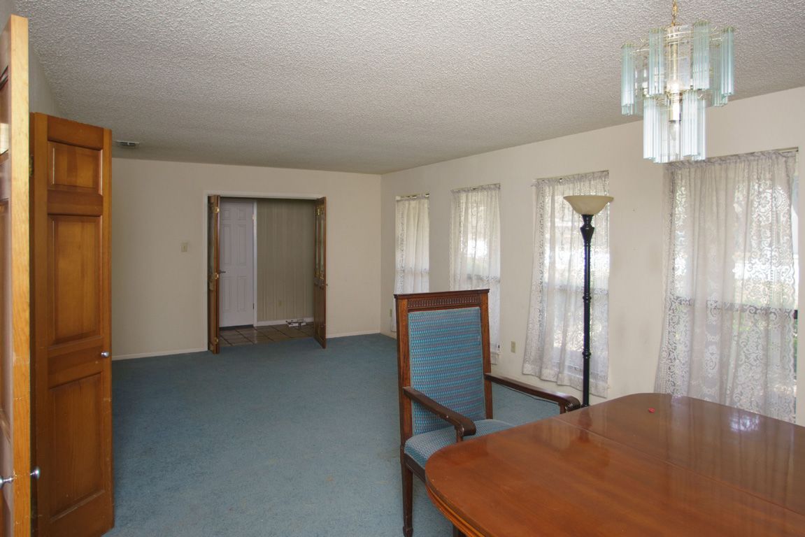 Dining room with blue carpet, wooden table, ornate chair, windows, and light fixture.