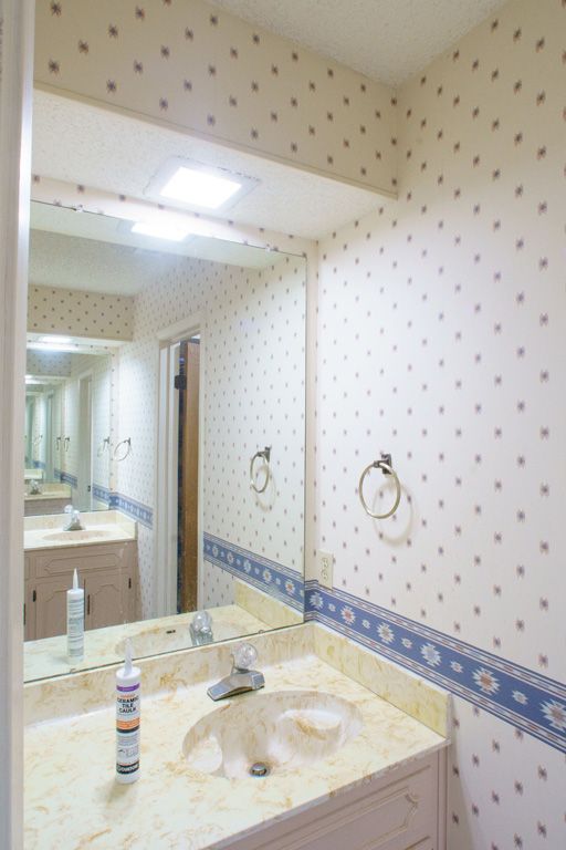 Bathroom with sink, mirror, and floral wallpaper. Beige marble countertop and blue floral border.
